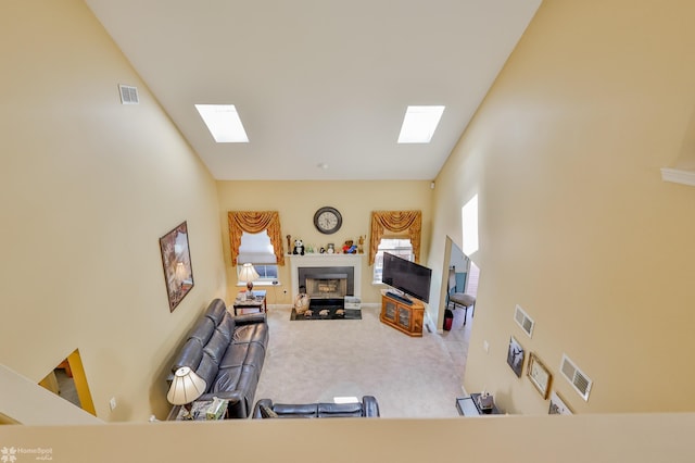 carpeted living area with a skylight, a fireplace with flush hearth, and a towering ceiling