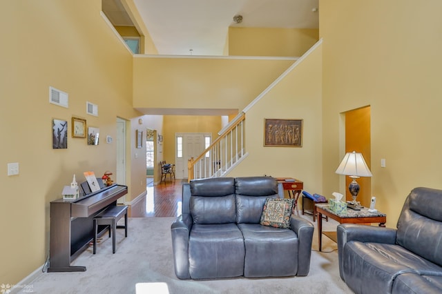 living room featuring a towering ceiling, stairs, light wood-style flooring, and baseboards