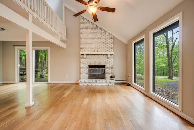 2166 Southport Dr, Bushkill, PA 18324 - unfurnished living room with a ceiling fan, light wood-style floors, a brick fireplace, a baseboard radiator, and high vaulted ceiling