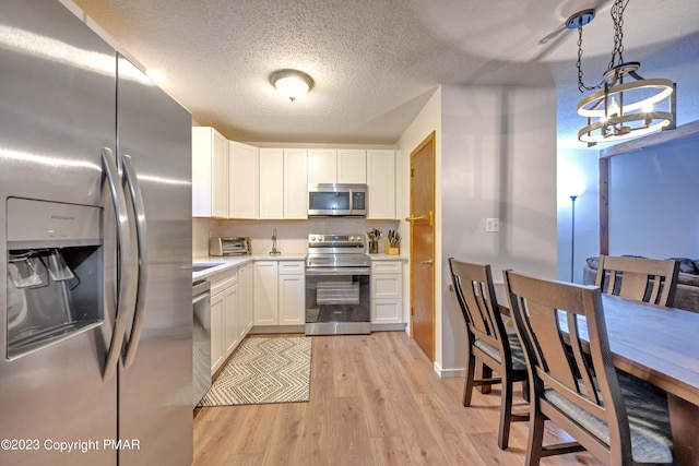 kitchen with white cabinets, light wood finished floors, appliances with stainless steel finishes, and light countertops