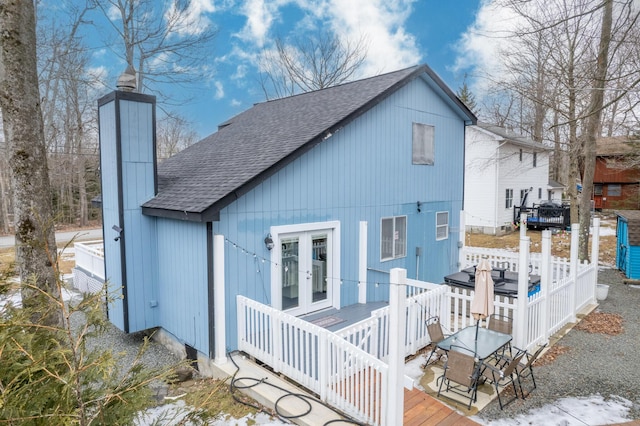 rear view of house featuring a shingled roof, a chimney, a deck, and french doors