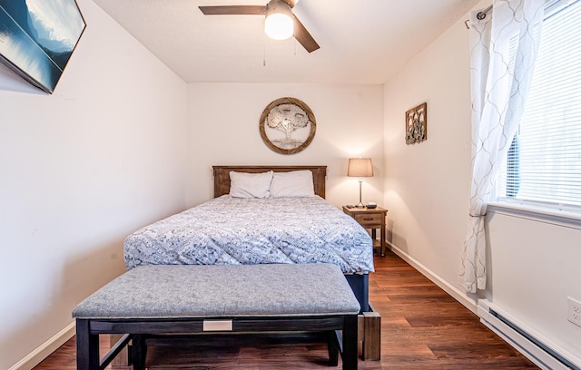 bedroom with a baseboard heating unit, dark wood-style flooring, and baseboards