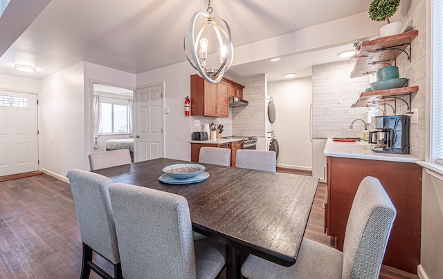 dining space featuring baseboards, dark wood-type flooring, and stacked washer and clothes dryer