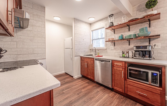 kitchen featuring stainless steel appliances, a sink, backsplash, brown cabinets, and dark wood finished floors