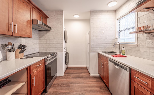 kitchen with brown cabinetry, stacked washer / drying machine, stainless steel appliances, under cabinet range hood, and a sink