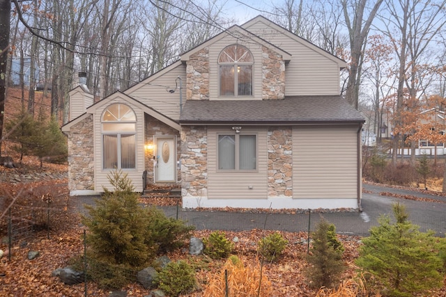 view of front of home featuring stone siding, a chimney, and a shingled roof