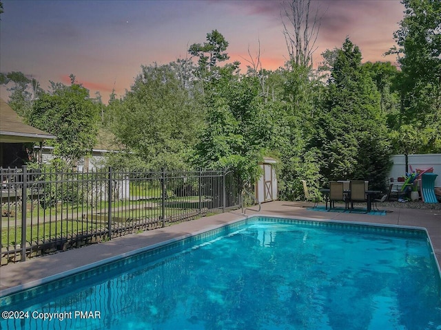 pool at dusk with a patio area, fence, and a fenced in pool