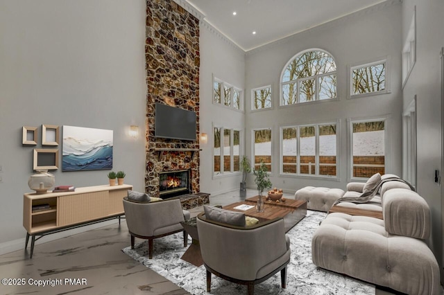 living room featuring a towering ceiling, marble finish floor, baseboards, and a stone fireplace