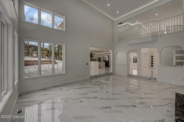 interior space with arched walkways, a towering ceiling, baseboards, marble finish floor, and ornate columns