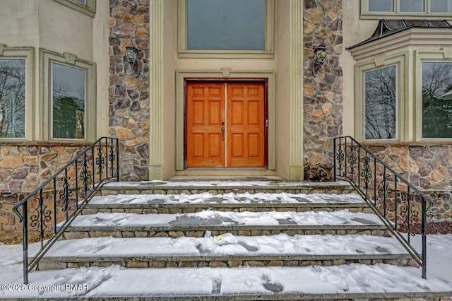 snow covered property entrance featuring stone siding