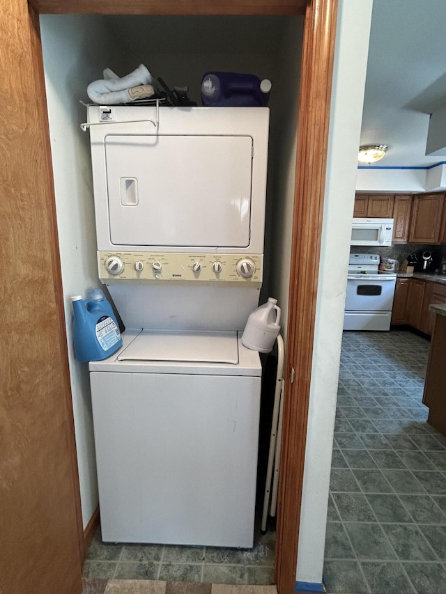 laundry room with dark tile patterned floors and stacked washer / dryer