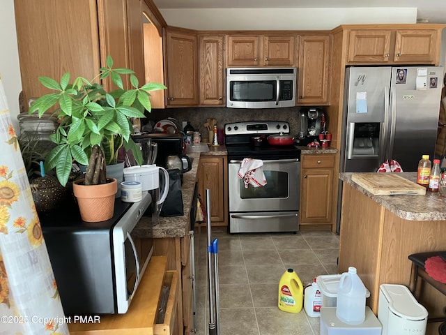 kitchen with appliances with stainless steel finishes, backsplash, brown cabinetry, and dark tile patterned floors