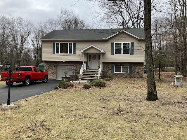 split foyer home featuring stone siding, an attached garage, driveway, and a shingled roof