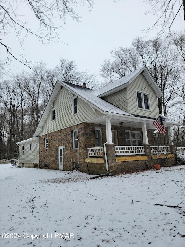 view of snow covered exterior with covered porch, a chimney, and stone siding