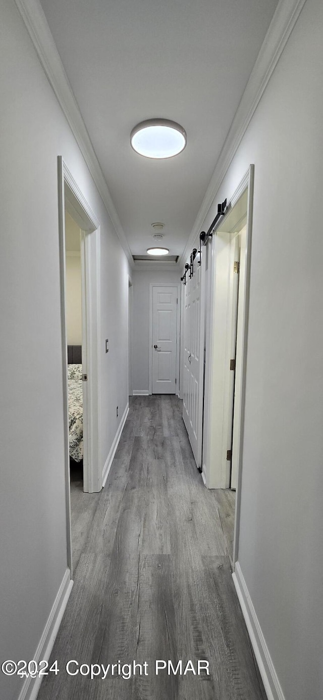 corridor featuring ornamental molding, wood finished floors, baseboards, and a barn door