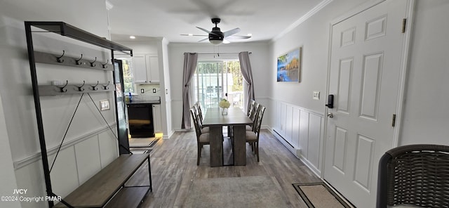 dining area with ceiling fan, a baseboard heating unit, a wainscoted wall, light wood finished floors, and crown molding