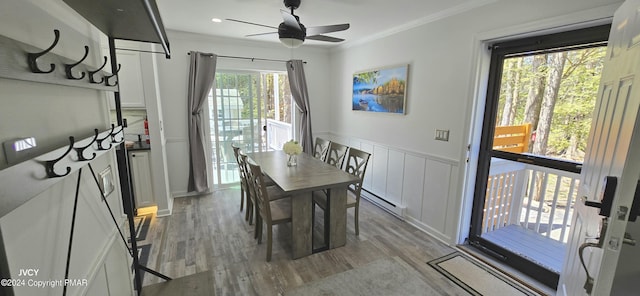 dining room featuring a baseboard heating unit, ornamental molding, wainscoting, and light wood-style floors