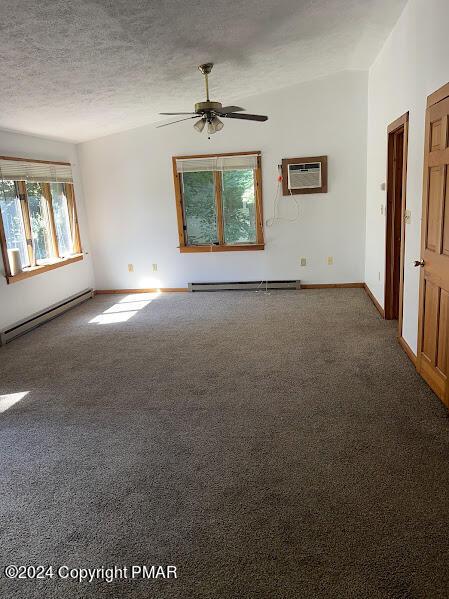 carpeted empty room featuring vaulted ceiling, baseboard heating, a textured ceiling, and a wall mounted air conditioner