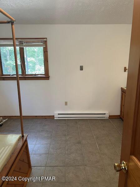 empty room featuring baseboards, a textured ceiling, baseboard heating, and tile patterned floors