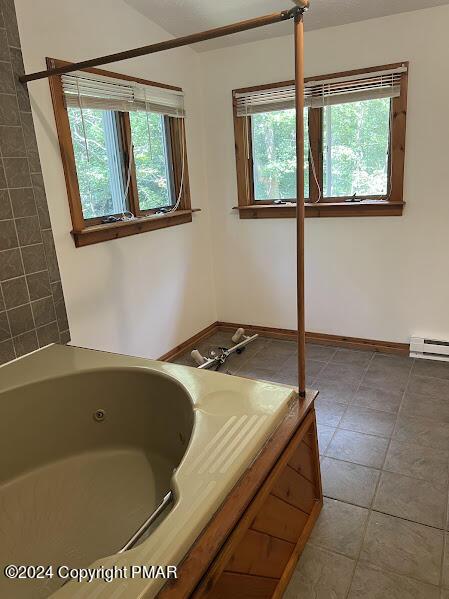 full bathroom featuring a baseboard heating unit, a wealth of natural light, tile patterned flooring, and a whirlpool tub