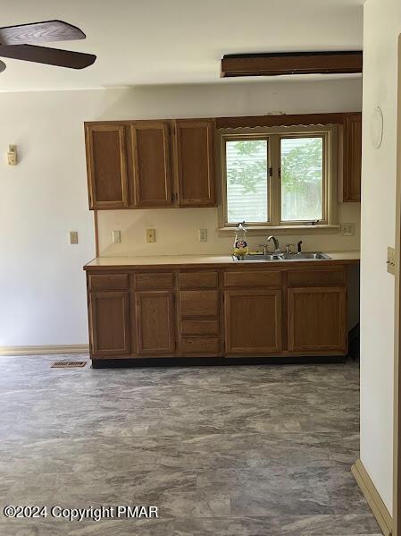 kitchen with light countertops, brown cabinetry, a ceiling fan, a sink, and baseboards