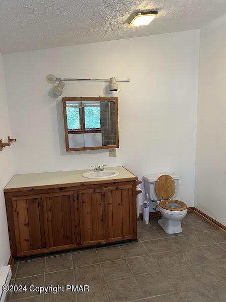 bathroom featuring a textured ceiling, toilet, a baseboard heating unit, vanity, and baseboards