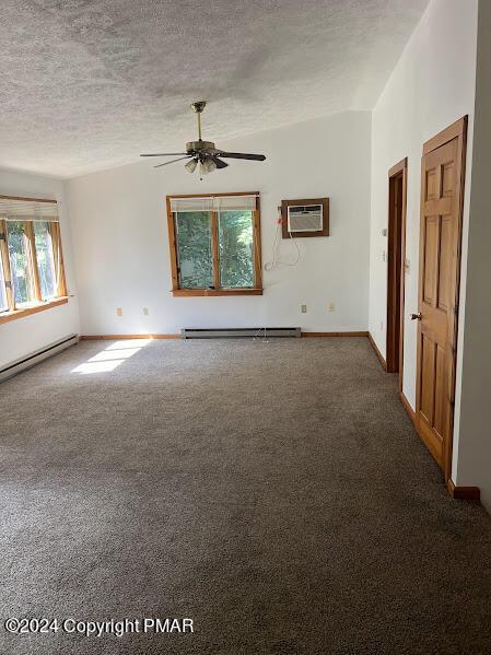 carpeted spare room with a textured ceiling, an AC wall unit, baseboard heating, and vaulted ceiling