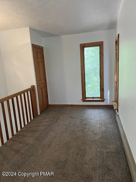 carpeted spare room featuring a textured ceiling and baseboards