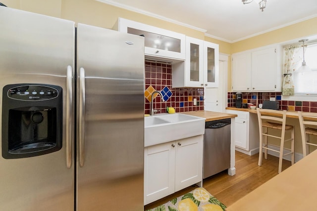 kitchen with ornamental molding, a sink, white cabinets, appliances with stainless steel finishes, and backsplash