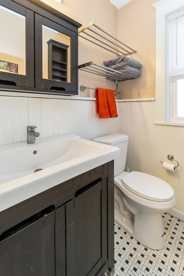 half bathroom featuring a wainscoted wall, toilet, vanity, and tile patterned flooring