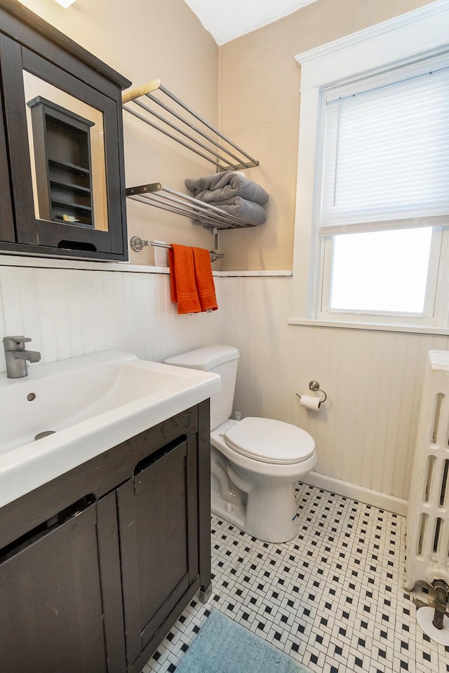 bathroom with toilet, radiator, vanity, and a wainscoted wall