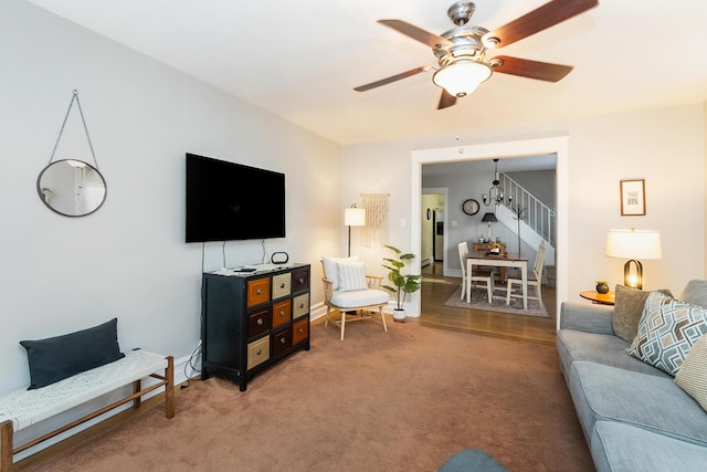 living room featuring light carpet, a ceiling fan, and stairs