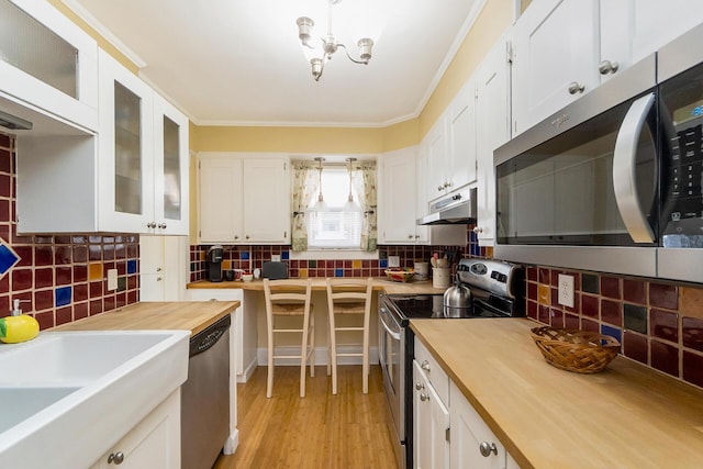 kitchen featuring white cabinetry, butcher block countertops, under cabinet range hood, and stainless steel appliances