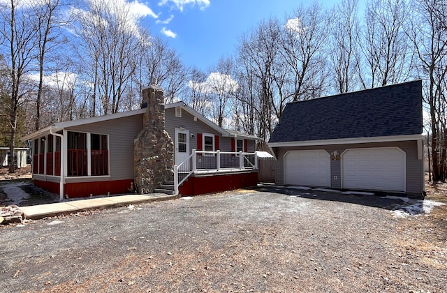 view of front of property with a detached garage, roof with shingles, an outdoor structure, a wooden deck, and a chimney