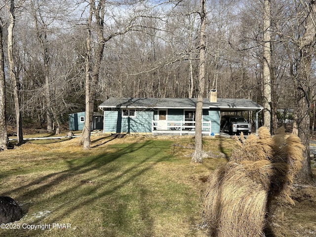 view of front facade with a forest view, an attached carport, a front lawn, and a chimney