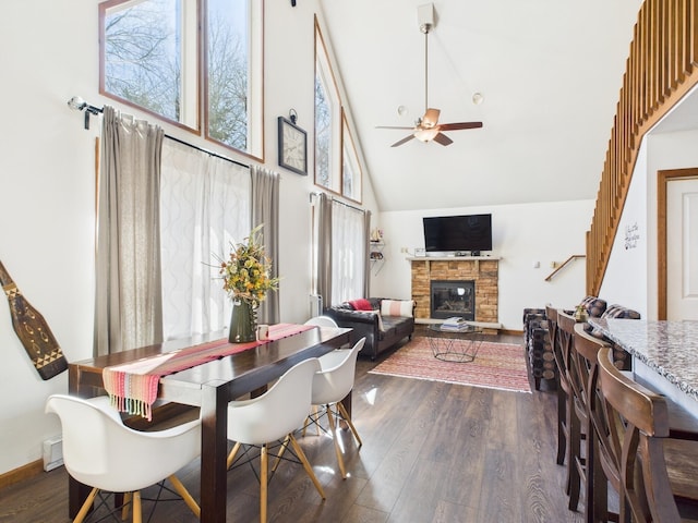 dining space with a fireplace, high vaulted ceiling, ceiling fan, and dark wood-style flooring