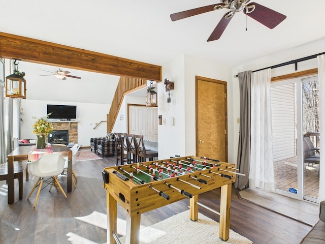 rec room with a stone fireplace, hardwood / wood-style flooring, vaulted ceiling with beams, and a ceiling fan