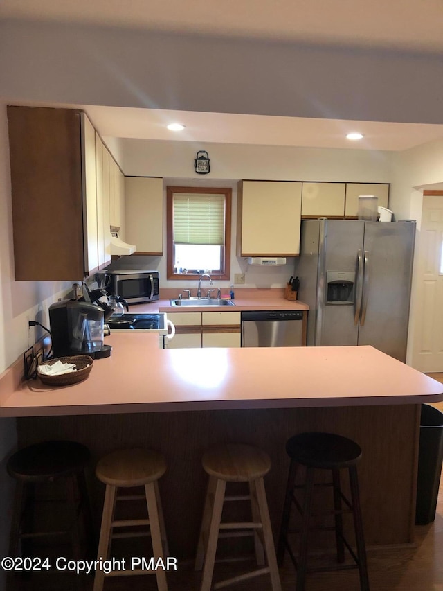 kitchen featuring a peninsula, stainless steel appliances, under cabinet range hood, a kitchen bar, and a sink