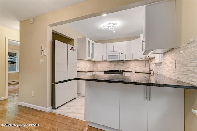 kitchen with a baseboard heating unit, a sink, dark stone countertops, white appliances, and a peninsula