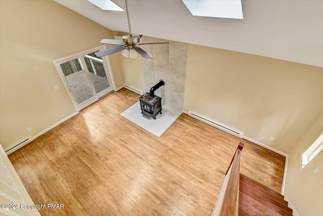 unfurnished living room featuring a skylight, a baseboard radiator, wood finished floors, a wood stove, and baseboard heating