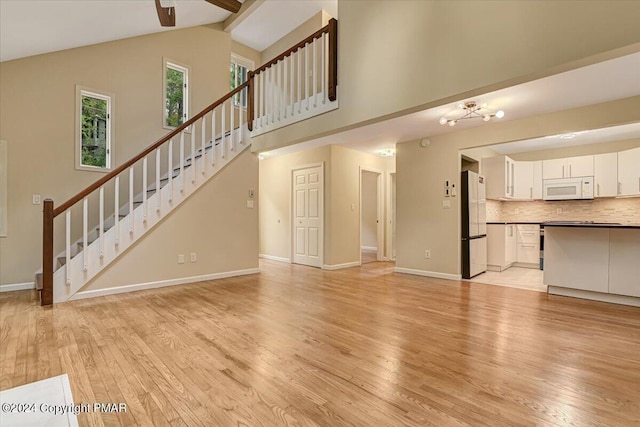 unfurnished living room with beam ceiling, stairway, light wood-style flooring, high vaulted ceiling, and baseboards