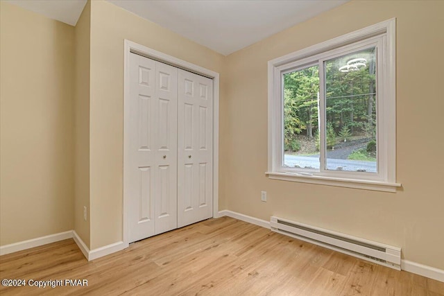 unfurnished bedroom with light wood-type flooring, a closet, baseboards, and baseboard heating