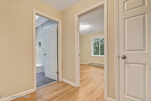 hallway with light wood-style floors, a baseboard radiator, and baseboards