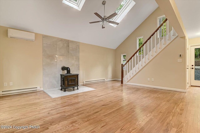 unfurnished living room with a skylight, wood finished floors, a wood stove, stairs, and high vaulted ceiling