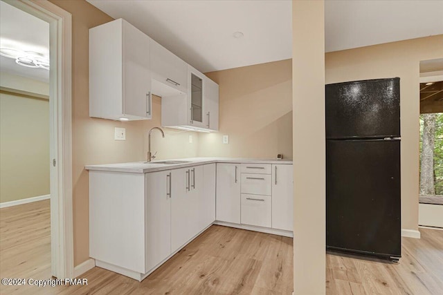 kitchen with freestanding refrigerator, white cabinets, a sink, and light wood-style flooring