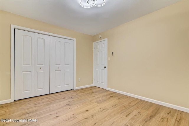 unfurnished bedroom featuring light wood finished floors, baseboards, and a closet