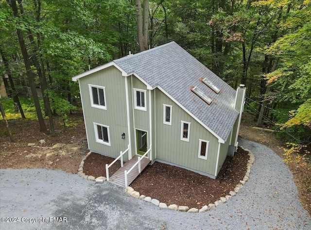 view of front of home featuring entry steps, a forest view, a shingled roof, and a chimney