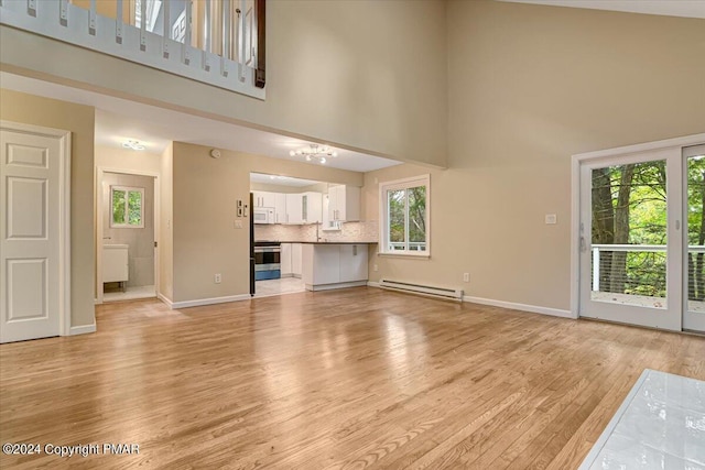 unfurnished living room with a baseboard heating unit, light wood-style floors, a towering ceiling, and baseboards