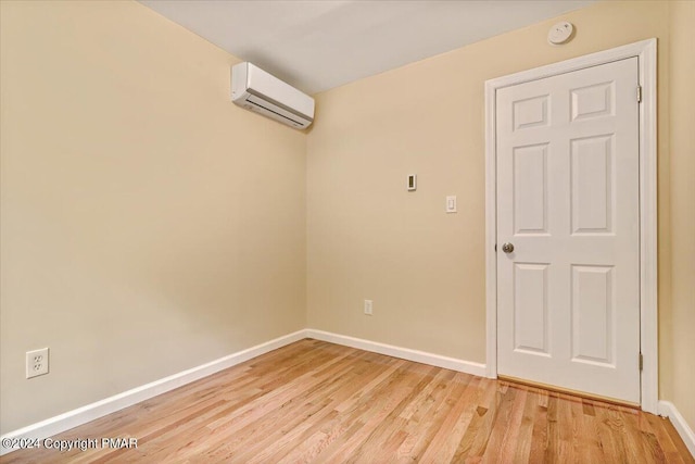 empty room with baseboards, a wall mounted air conditioner, and light wood finished floors