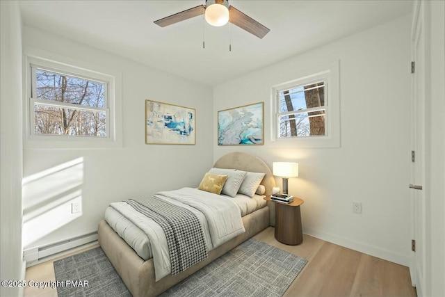 bedroom with baseboard heating, ceiling fan, multiple windows, and light wood-type flooring